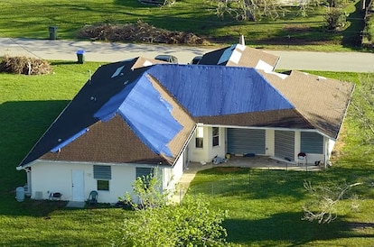 Hurricane Ian damaged house rooftop covered with protective plastic tarp against rain water leaking